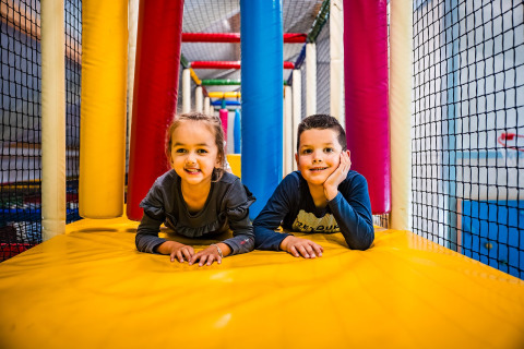 Zwei Kinder spielen lächelnd auf einem bunten Indoor-Spielplatz im Zweedse Huisjes im Beloofde Land, Niederlande.