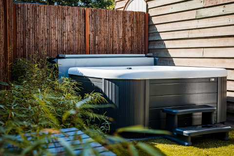 Outdoor hot tub next to a wooden fence and green plants at Zweedse Huisjes, Beloofde Land, Netherlands.