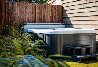 Outdoor hot tub next to a wooden fence and green plants at Zweedse Huisjes, Beloofde Land, Netherlands.