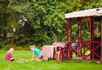 Two children play on the grass outside a cozy cabin with a bike at Zweedse Huisjes in Beloofde Land, Netherlands.