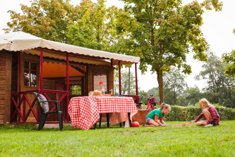 Kinder spielen auf dem Rasen vor einer gemütlichen Hütte mit rotweißem Tisch in Zweedse Huisjes, Niederlande.