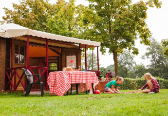 Bambini giocano sull’erba vicino a un lodge accogliente con tavolo a quadretti in Zweedse Huisjes, Beloofde Land.