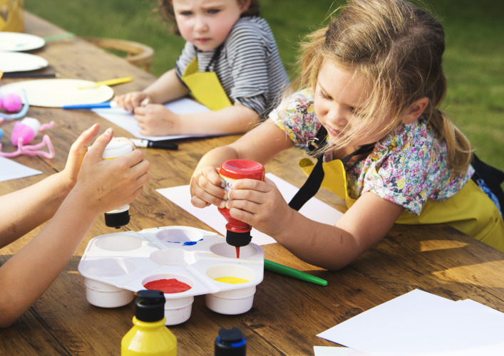 Kinderen schilderen met verf aan een houten tafel buiten bij Konijntje huisje, Beloofde Land, Nederland.