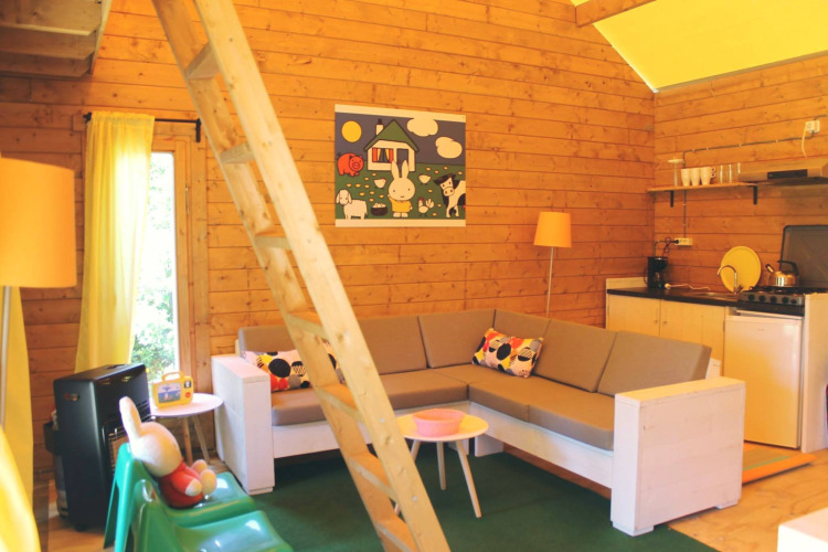 Interno di una tenda safari Konijntje huisje, con pareti in legno, divano ad angolo e piccola cucina.