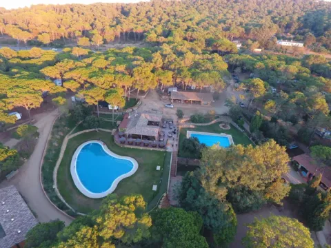 Aerial view of Camping Begur in Catalonia, Spain, featuring swimming pools, buildings, and surrounding forest.