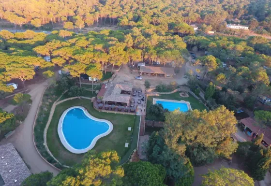 Vista aérea del Camping Begur en Cataluña, España, con piscinas, edificios y bosque circundante.