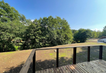 View from wooden deck at Ecolodge - Zorgtoegankelijk, Hameau de l'Ourthe, Belgium with sunny sky.