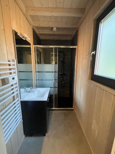 Baño moderno con paneles de madera, ventana grande, lavabo y ducha en Ecolodge en Hameau de l'Ourthe, Bélgica.
