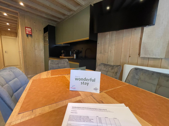 Binnenzicht van Ecolodge bij Hameau de l'Ourthe, België, met tafel, stoelen, tv en welkomstkaart.