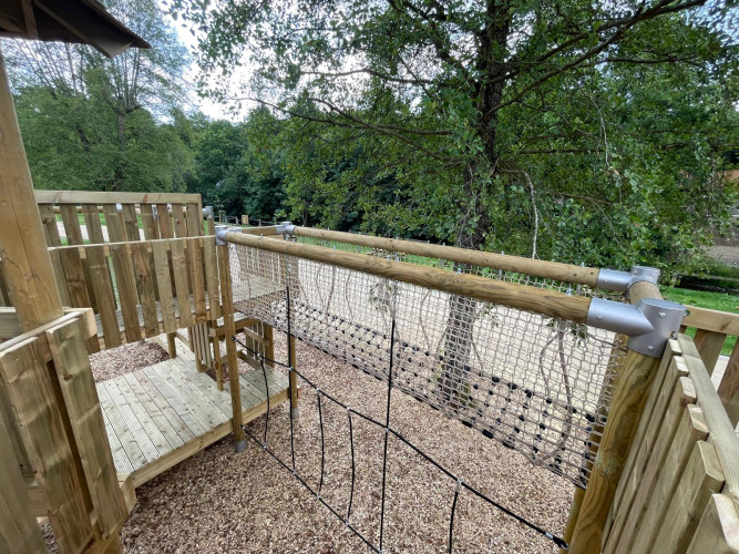 Terraza de madera con red de escalada y vistas a árboles, foto tomada en un glamping.