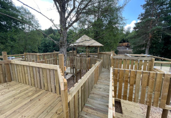 Pasarela y terraza de madera en alojamiento glamping, rodeado de árboles y vegetación en el bosque.