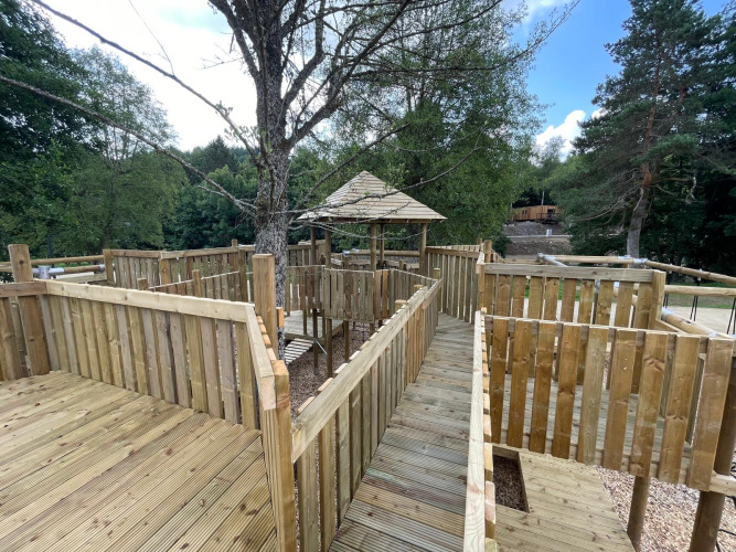 Passerelle et terrasse en bois dans un hébergement glamping, entourées d’arbres et de verdure en forêt.