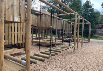 Parque infantil de madera con estructuras para escalar en un alojamiento glamping rodeado de naturaleza.
