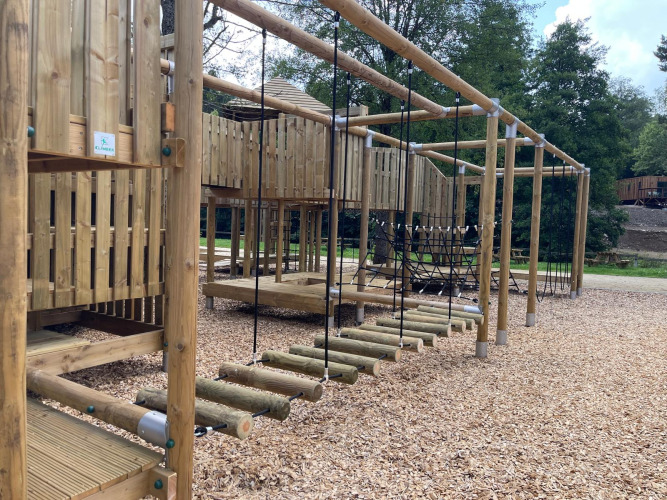 Parque infantil de madera con estructuras para escalar en un alojamiento glamping rodeado de naturaleza.