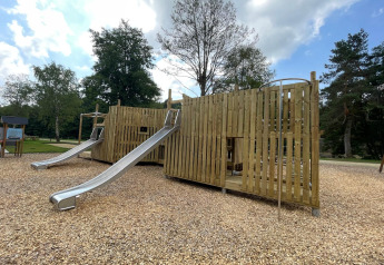 Parque infantil con estructuras de madera y toboganes metálicos en un entorno de glamping rodeado de árboles.