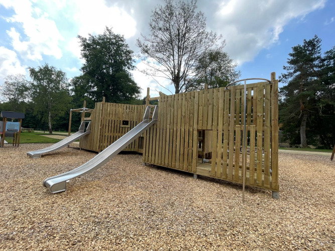 Aire de jeux avec structures en bois et toboggans métalliques, située dans un site de glamping arboré.