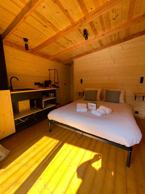Interieur van een boomhut in Hameau de l'Ourthe, België, met houten afwerking, een bed en invallend zonlicht.