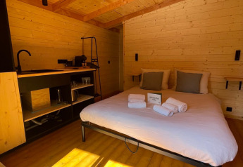 Interior de una casa en el árbol en Hameau de l'Ourthe, Bélgica, con paneles de madera, cama y luz solar.
