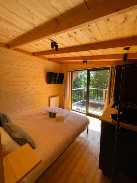 Binnenkant van de boomhut bij Hameau de l'Ourthe in België met houten interieur, bed en balkon met zicht.