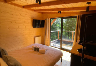 Binnenkant van de boomhut bij Hameau de l'Ourthe in België met houten interieur, bed en balkon met zicht.