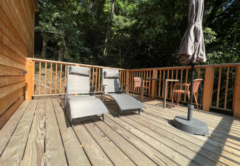 Terraza soleada de madera con tumbonas y sombrilla en Tree House at Hameau de l'Ourthe en Bélgica, rodeada de bosque.