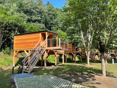 Boomhut bij Hameau de l'Ourthe in België, tussen bomen, met houten trap en ruim terras.