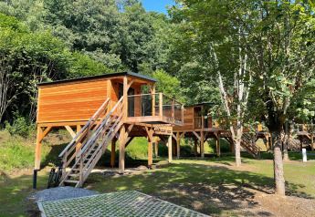 Casa del árbol en Hameau de l'Ourthe, Bélgica, rodeada de vegetación con escaleras y terraza de madera.