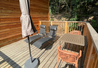 Terraza de madera con sillas y mesa en la Tree House del Hameau de l'Ourthe, Bélgica, rodeada de árboles.