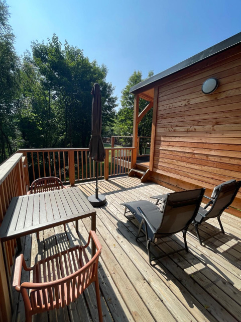 Houten terras aan de Tree House in Hameau de l'Ourthe in België met stoelen, tafel en ligstoelen.