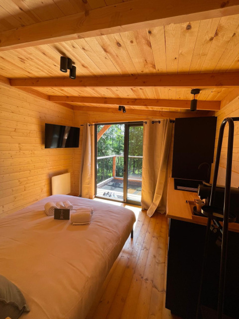 Knusse slaapkamer in de boomhut van Hameau de l'Ourthe, België, met houten interieur en zicht op het bos.