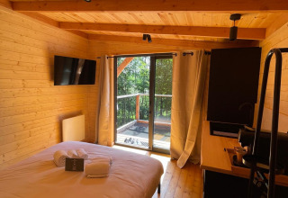 Knusse slaapkamer in de boomhut van Hameau de l'Ourthe, België, met houten interieur en zicht op het bos.