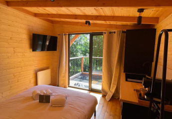 Acogedor dormitorio en la casa del árbol de Hameau de l'Ourthe, Bélgica, con interior de madera y vista al bosque.