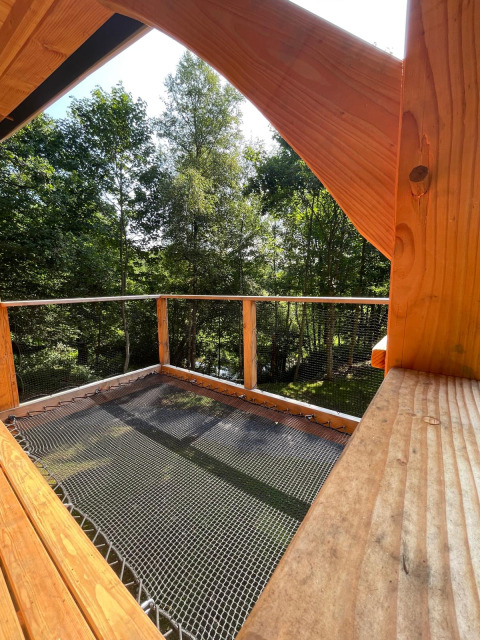 Uitzicht vanop een boomhut aan Hameau de l'Ourthe in België, met houten terras, net en groene bomen.