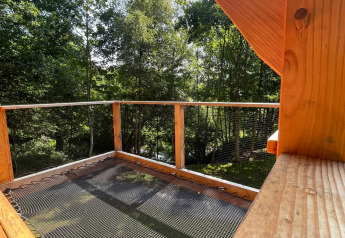 Vista desde una casa en el árbol en Hameau de l'Ourthe, Bélgica, con balcón de madera, red y paisaje boscoso.