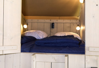 Ingresso a una zona notte accogliente in una tenda safari con pareti in legno, scala e lenzuola blu.