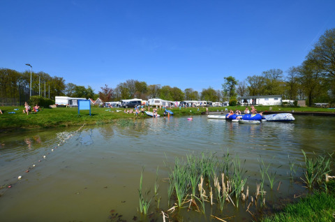 Kinderen spelen en zwemmen in een vijver omringd door gras en caravans op Vakantiepark De Witte Berg.