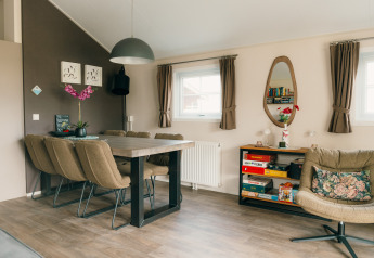 Salon moderne avec table à manger, six chaises, fauteuil et étagère, lodge Veluwe au parc De Boshoek, Pays-Bas.