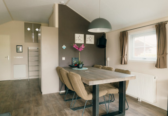 Dining area with modern table, six chairs, and large windows in Veluwe lounge + sauna, De Boshoek, Netherlands.