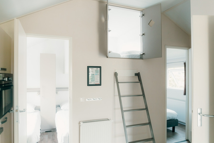 Vista interior de la lodge Veluwe lounge + sauna en Holiday park De Boshoek con escalera hacia altillo.