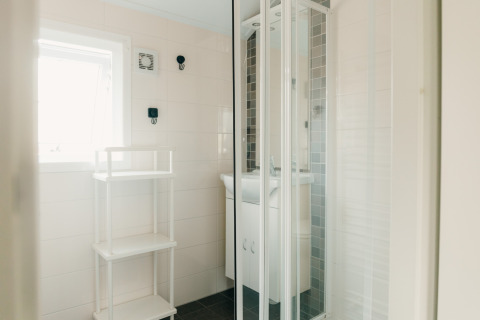 Helles Badezimmer in der Veluwe lounge + sauna im Holiday park De Boshoek mit Duschkabine und Regal.