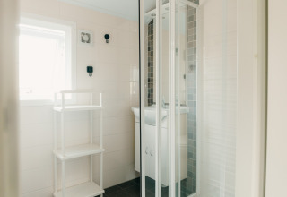 Lyst badeværelse i Veluwe lounge + sauna på Holiday park De Boshoek med brusekabine og reol.