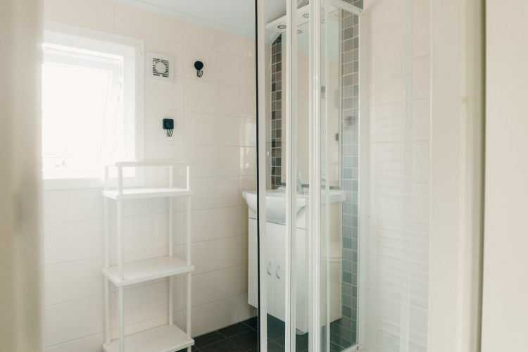 Baño luminoso en Veluwe lounge + sauna en Holiday park De Boshoek, con ducha y estantería blanca.