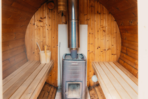 Indvendigt billede af træsauna med varmeovn, bænke og spand på Veluwe lounge + sauna i Holland.