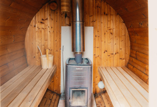 Vista interior de una sauna de madera con estufa, bancos y cubo en Veluwe lounge + sauna en Países Bajos.