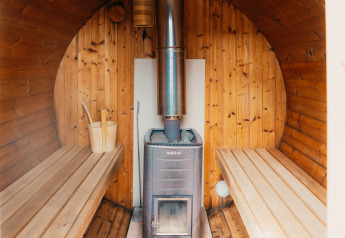 Indvendigt billede af træsauna med varmeovn, bænke og spand på Veluwe lounge + sauna i Holland.