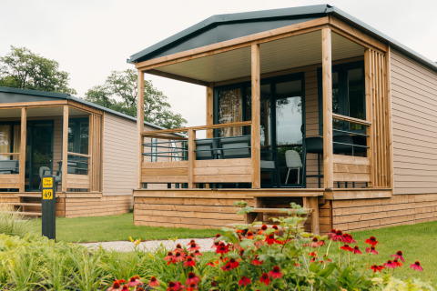 Gemütliche Tiny Lodges im Holiday park De Boshoek, Niederlande, mit Holzveranda und bunten Blumen im Vordergrund.