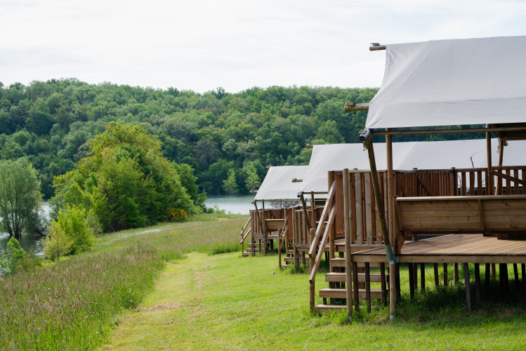 Tende glamping safari al Domaine La Barbe in Francia con vista su bosco rigoglioso e lago tranquillo.