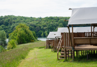 Safari glamping tents at Domaine La Barbe in France overlooking lush forest and a tranquil lake.