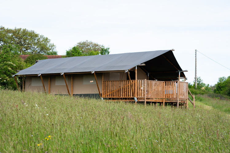 Glamping safari tent at Domaine La Barbe in France, set in a grassy field with wooden deck and nature.