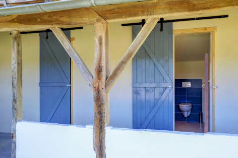 Buitenbadkamers met blauwe schuifdeuren en zichtbaar toilet aan de glampingtent bij Domaine La Barbe.